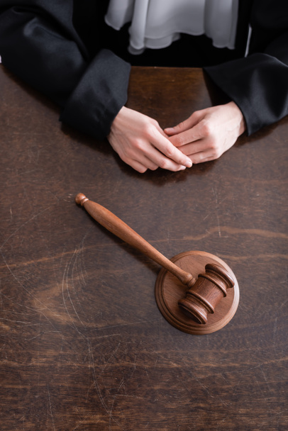 partial view of judge sitting near wooden gavel on desk - Фото, изображение