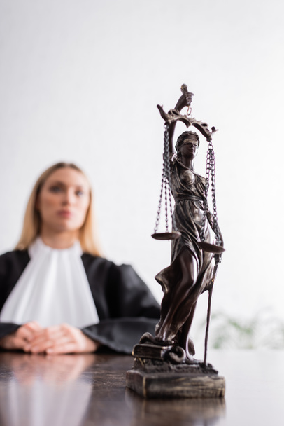selective focus of themis statue near prosecutor in mantle sitting on blurred background - Foto, immagini