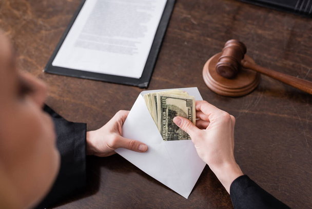 partial view of prosecutor with bribe in envelope near blurred gavel on desk - Фото, зображення