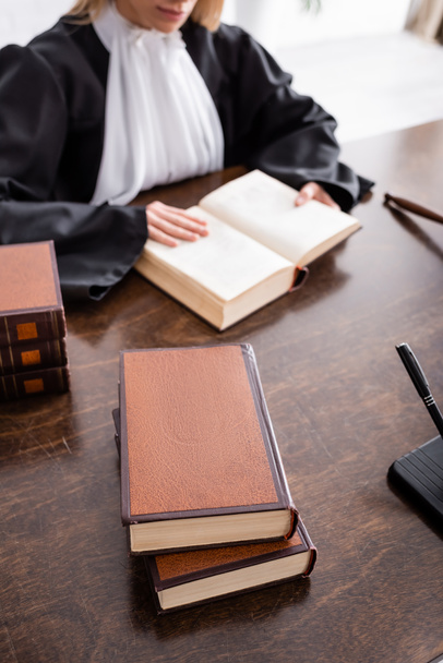 bijgesneden weergave van wazig officier van justitie die juridische literatuur leest in de buurt van boeken op houten bureau - Foto, afbeelding