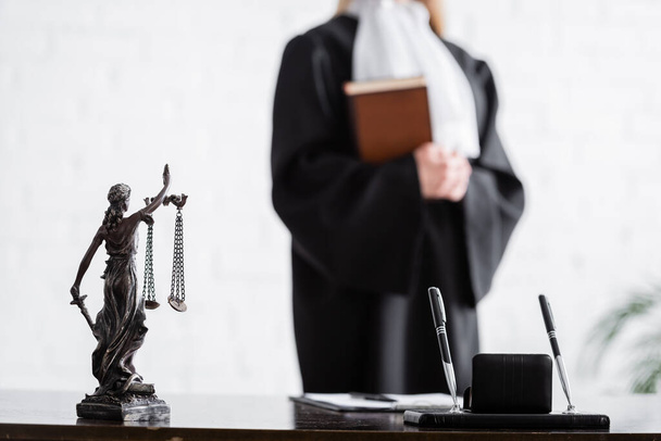 selective focus of themis statue and pens near cropped prosecutor with book on blurred background - Фото, зображення