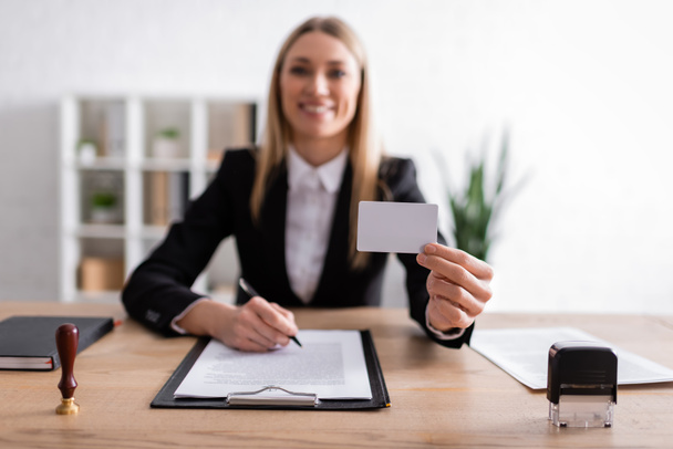 happy notary holding blank business card while sitting on blurred background - Fotoğraf, Görsel
