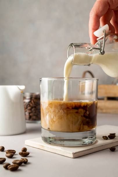 Pouring milk in glass with iced coffee. Cold refreshment summer sweet drinks - 写真・画像