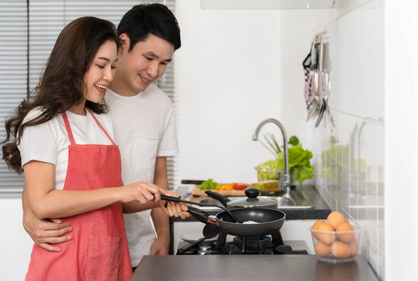 happy young couple cooking and preparing food in the kitchen at home. man in hugging woman - Foto, Imagem