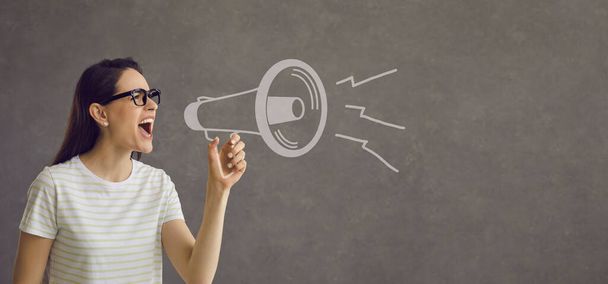 Serious woman draws attention to an important event by shouting loudly into a loudspeaker. - 写真・画像