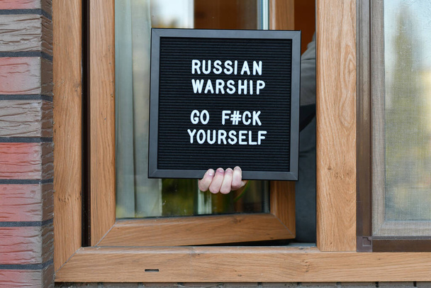 Mano sosteniendo un buzón en la ventana con la cita "Buque de guerra ruso go f # ck yourself". Guerra en Ucrania. - Foto, Imagen