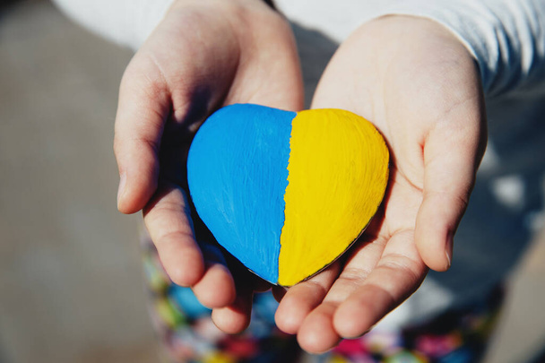 Small little kid hold heart shaped stone with Ukraine national flag or anthem - Foto, Imagem