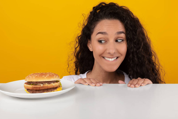Hungrige Dame schaut auf Burger, der aus Tisch guckt - Foto, Bild