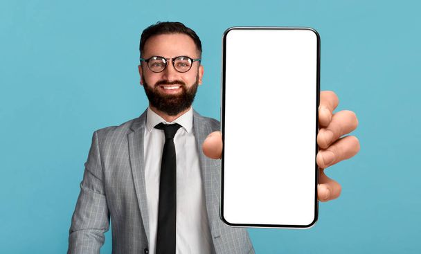 Oferta móvil. Hombre de negocios guapo sosteniendo el teléfono móvil con la pantalla vacía, mostrando el dispositivo con la maqueta - Foto, Imagen