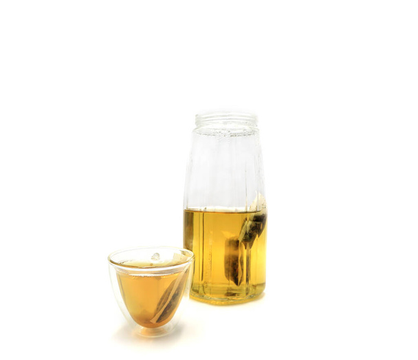 Átlátszó üveg kancsó és csésze gyógynövény tea fehér alapon. - Fotó, kép