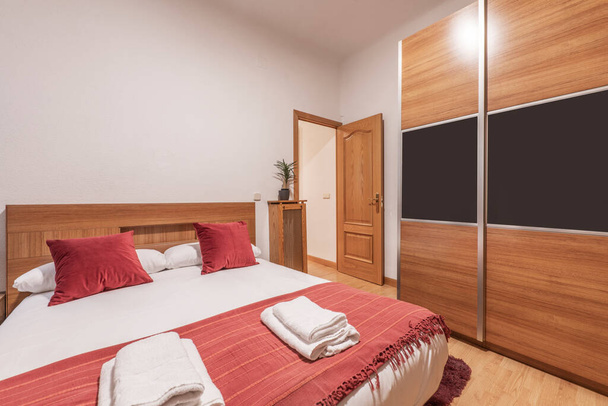 Bedroom with king size bed, red cushions, matching blanket, white bedding and wooden sliding door wardrobe - Valokuva, kuva