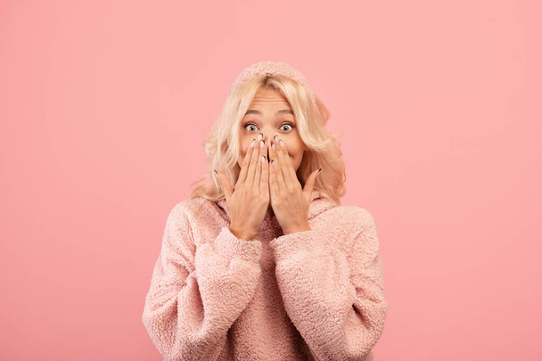 Human emotions concept. Shocked lady covering her mouth with hands and looking at camera, pink background - Photo, Image