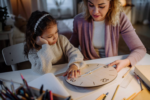 Happy little girl learning time with wooden clock with her mother in evening at home. - Foto, Imagem