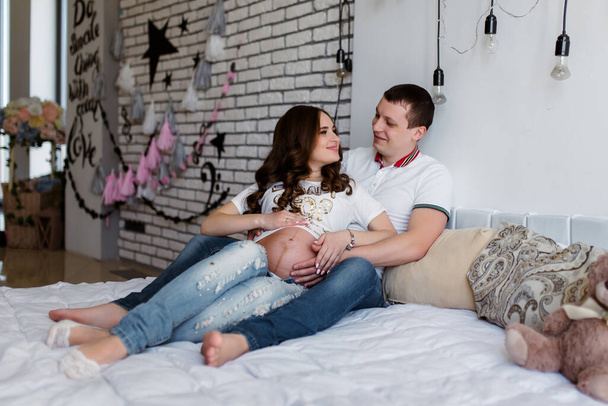 Schwangerschaft und Menschen-Konzept - glücklicher Mann umarmt seine schwangere Frau, die zu Hause am Fenster steht - Foto, Bild