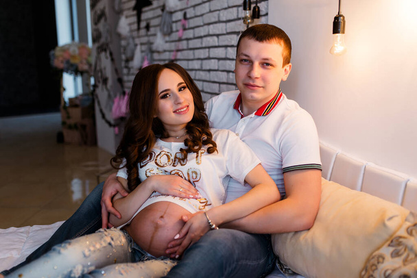 Photo of happy expecting couple sit on couch touch belly closed eyes imagine parenthood indoors in living room - Фото, изображение