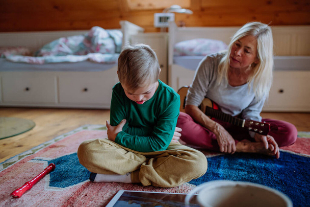 Boy with Down syndrome sitting on floor and playing with his grandmother at home - Photo, Image