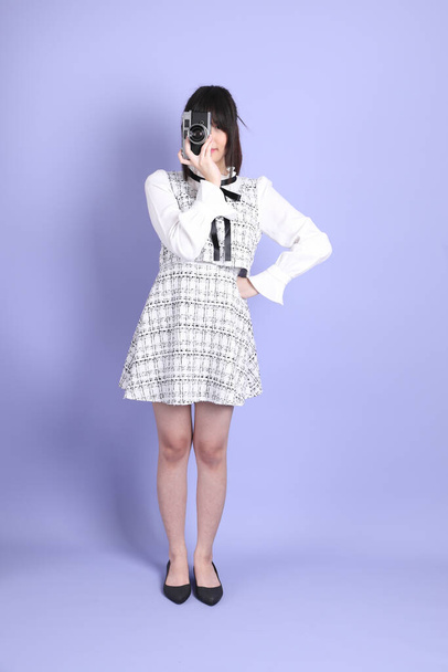 La giovane ragazza asiatica in bianco preppy vestita in piedi sullo sfondo viola. - Foto, immagini