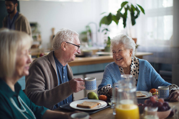 Group of cheerful seniors enjoying breakfast in nursing home care center. - Фото, изображение
