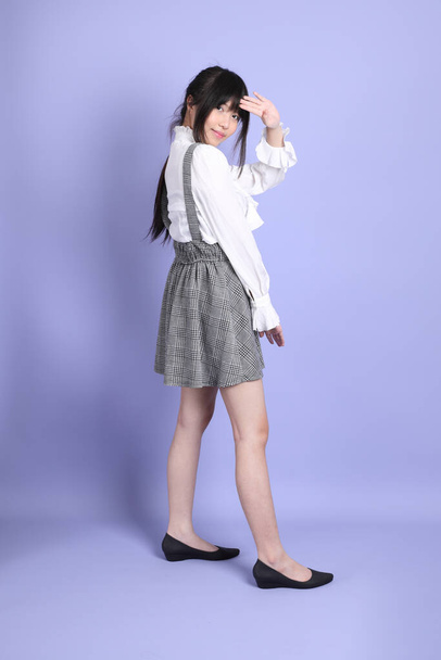 La joven chica asiática linda con preppy blanco vestido estilo de pie sobre el fondo púrpura - Foto, imagen