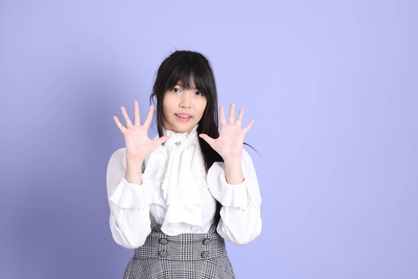 The cute young Asian girl with white preppy dressed style standing on the purple background - Foto, Imagen