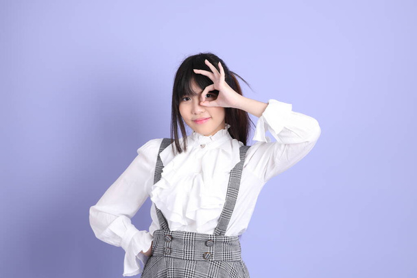The cute young Asian girl with white preppy dressed style standing on the purple background - Foto, Imagen