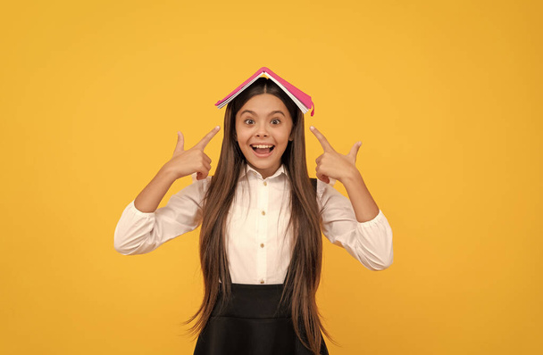 happy teen girl in school uniform pointing finger book on head, learn - Фото, изображение