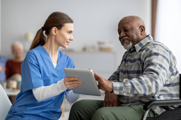 Friendly nurse helping black senior man using digital tablet - Foto, imagen