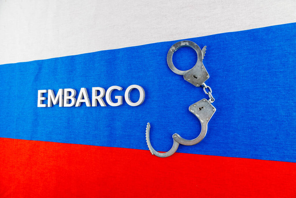 the word embargo laid with silver metal letters on russian tricolor flag with silver handcuffs - Foto, Imagen