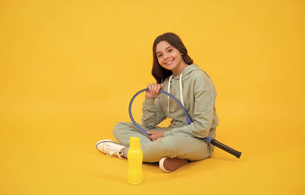 šťastný dítě sedět s tenisovou raketou a láhev vody na žlutém pozadí, zdravý životní styl. - Fotografie, Obrázek