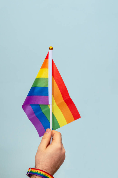 Man's hand holding Lgtb rainbow flag on blue background. Lgtb movement.  - Photo, Image
