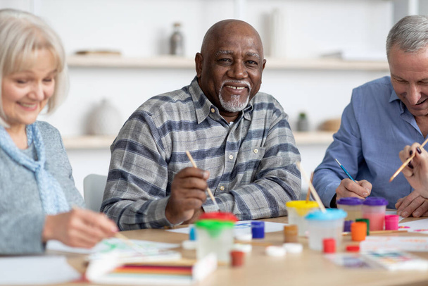 Feliz hombre negro senior disfrutando de la actividad de pintura con sus amigos - Foto, imagen