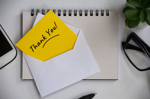 Thank you note on yellow paper in an envelope with office background concept. Appreciation concept - Photo, Image