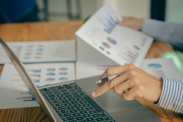 egy üzletember ül egy asztalnál, elemzi a pénzügyi diagramot tollal a kezében A könyvelők olyan adatlapokkal dolgoznak, amelyeket üzleti jelentésekben számolnak ki. egy laptoppal az irodában - Fotó, kép