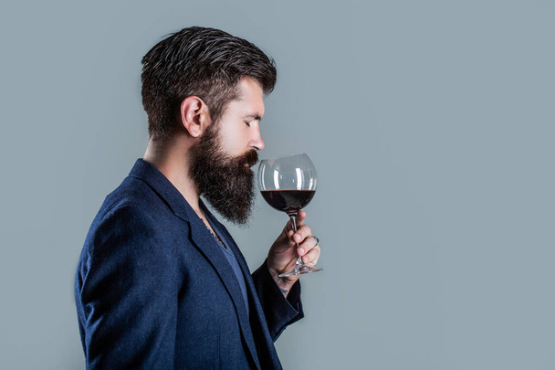 Человек с бокалом красного вина в руках. Бородач, бородатый, сомелье пробует красное вино. Соммелье, дегустатор с бокалом вина, винодельня, винодел-мужчина - Фото, изображение