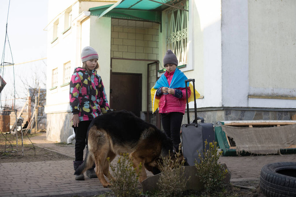 ウクライナ軍の移住。スーツケースを着た2人の少女。ウクライナの国旗,助けて.危機、武力紛争 - 写真・画像