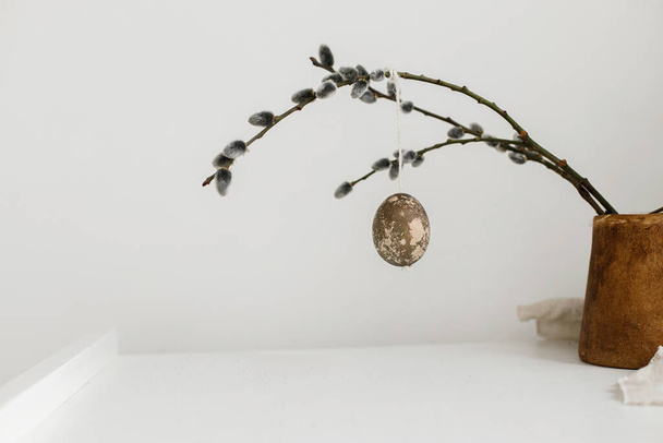 Frohe Ostern! Ostern rustikales minimalistisches Stillleben. Natürliche Ostereier hängen an Weidenzweigen auf einem Holztisch. Schlichte, stilvolle Osterdekoration auf der Tischästhetik - Foto, Bild