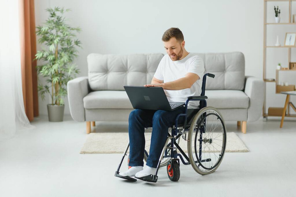 Work at home. Paralyzed male person holding laptop on knees and keeping smile on face while looking at screen - 写真・画像