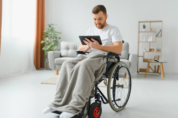 Nowoczesny młody niepełnosprawny mężczyzna na wózku inwalidzkim mając wideo połączenie - Zdjęcie, obraz