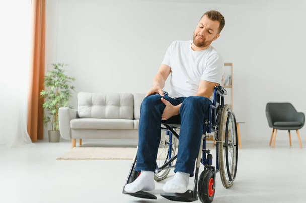 disabled man at home tries to get to his feet in a wheelchair. The concept of rehabilitation after injuries and car accidents. - Zdjęcie, obraz