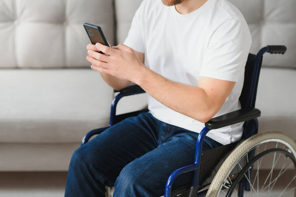 Young happy entrepreneur in wheelchair reading message on smart phone at home. - Fotó, kép