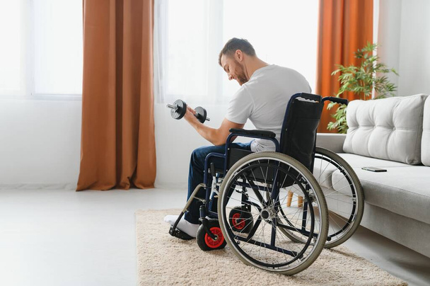 Man Disabled. Sports for Disabled. Male in Wheelchair with Dumbbells in Hands. Man with Dumbbells in Hands. Father Disabled Do Spotting. Sport at Apartment. Health Concept. Healthy Lifestyle. - Photo, Image