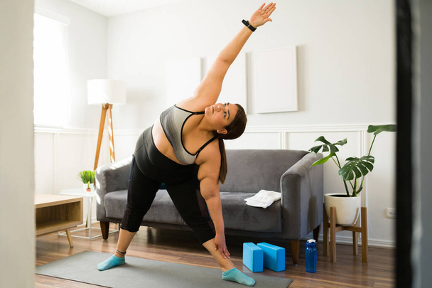 Mujer obesa activa en ropa deportiva estirándose mientras comienza su entrenamiento en casa para perder peso - Foto, imagen