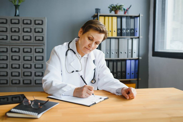 Mid age female doctor writing prescription - Фото, изображение