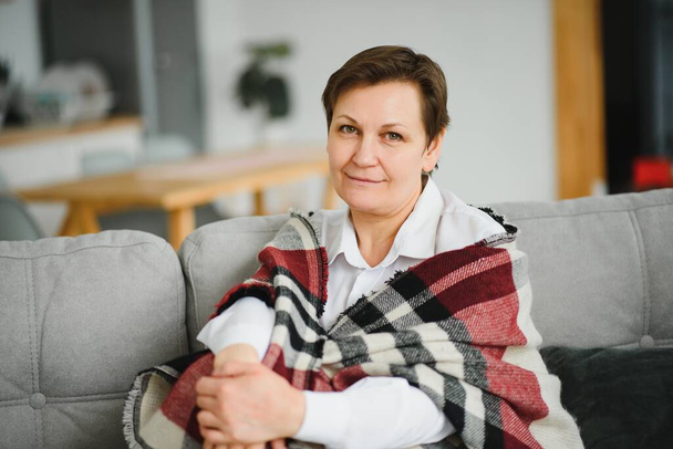 portrait of senior woman at home on sofa with plaid - Fotó, kép