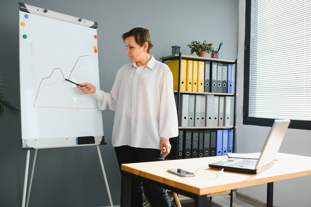 Mature older businesswoman mentor coach training speaker give flip chart business presentation at company meeting, confident female executive manager teaching team consult clients at office workshop - Foto, Imagen