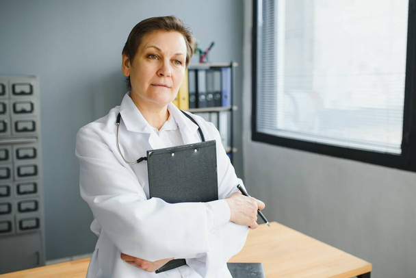 Portrait de femme médecin d'âge moyen porte un manteau de médecin blanc avec un stéthoscope autour du cou. - Photo, image