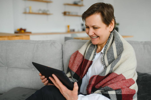 portrait of beautiful old woman using tablet pc and smiling, sitting on sofa at home - Foto, immagini