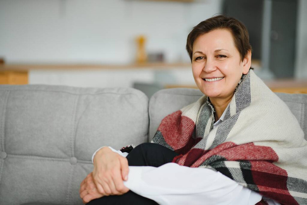 Mature Woman. Beautiful Healthy Middle Age Female Sitting On Sofa At Home. Beauty And Comfort Concept. - Fotografie, Obrázek