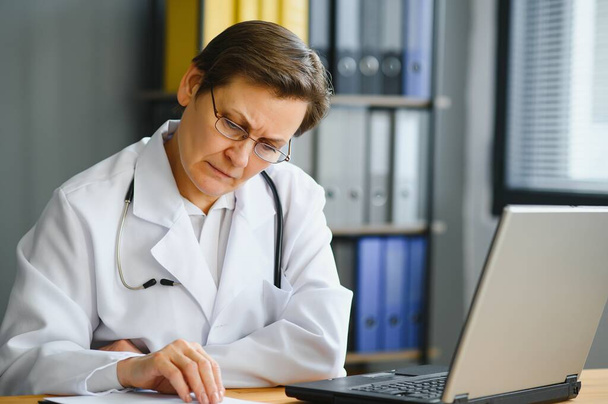 Portrait of mature female doctor in white coat at workplace - Foto, Imagen