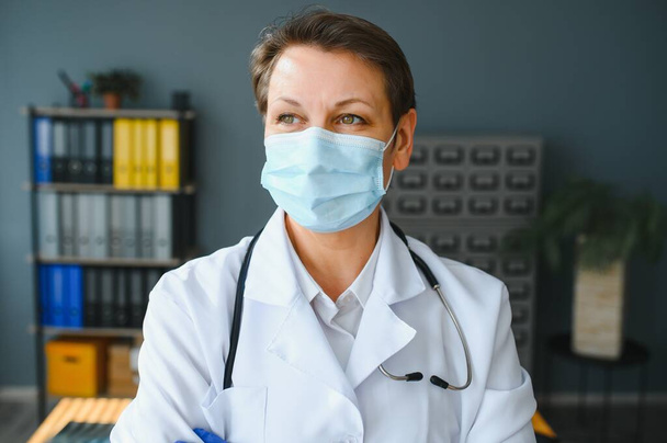 Portrait of a female doctor wearing face mask and holding her patient chart on digital tablet while standing at the hospital. - Foto, afbeelding